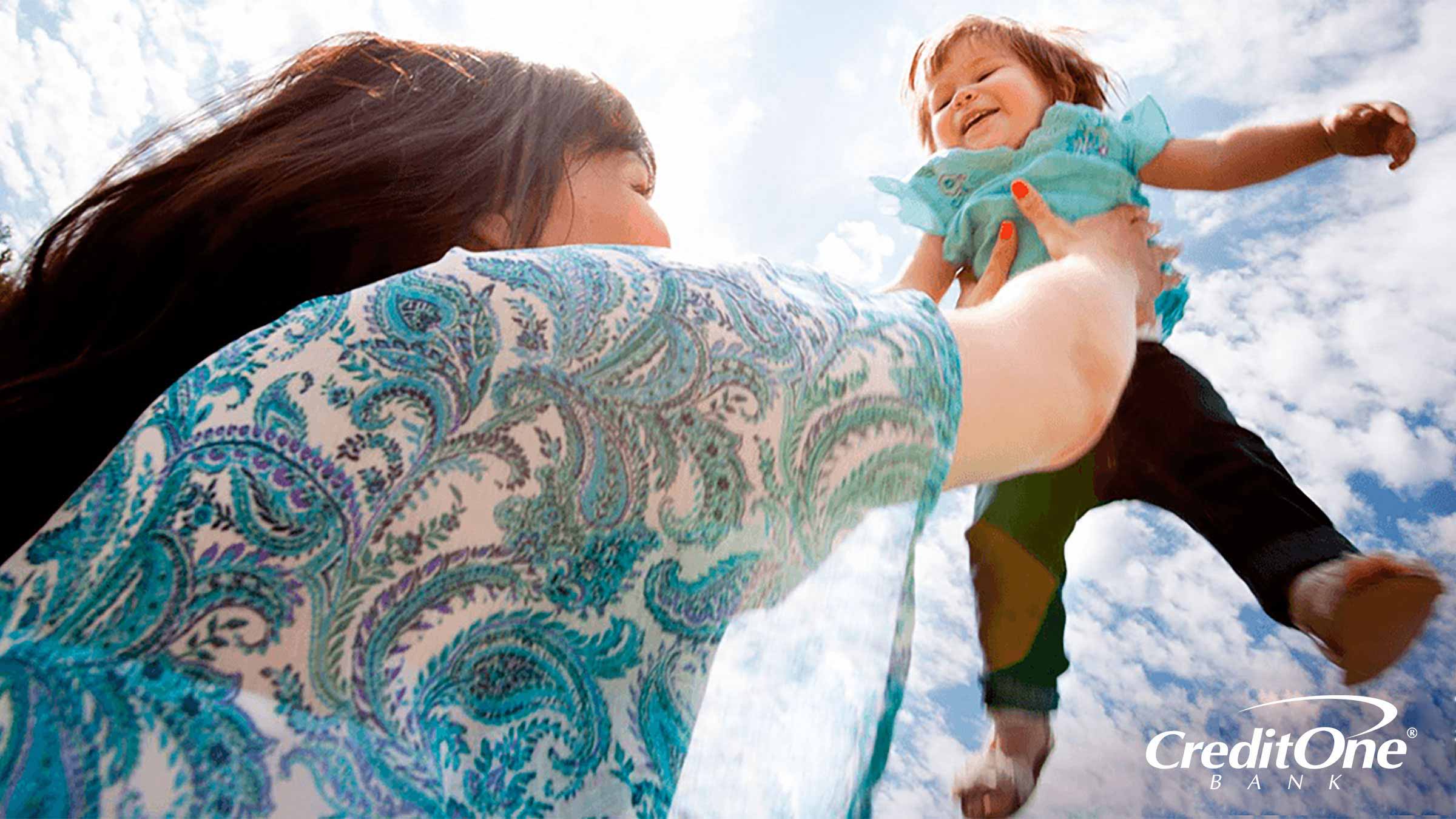 A mom lifts her young child high into the air, representing long-term financial goals for her family.