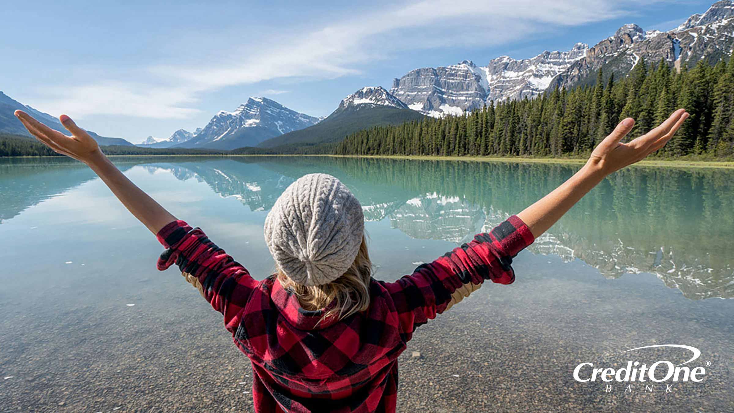 Woman with arms spread wide overlooking a lake and mountain range