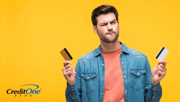 A confused young man holds up two credit cards, trying to choose the best credit card for him.