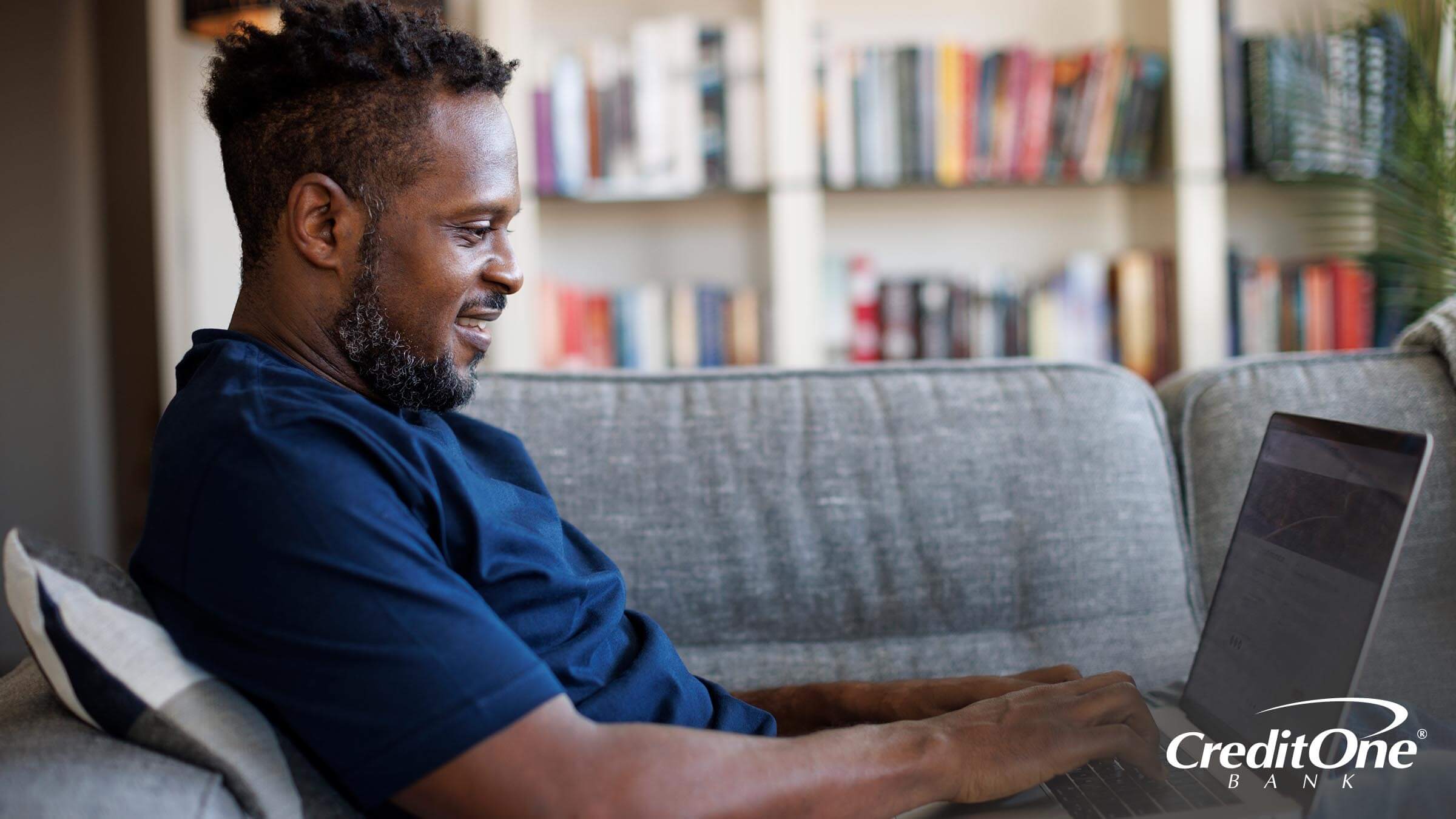 A man sitting at his couch and using his laptop to apply for a credit card. 