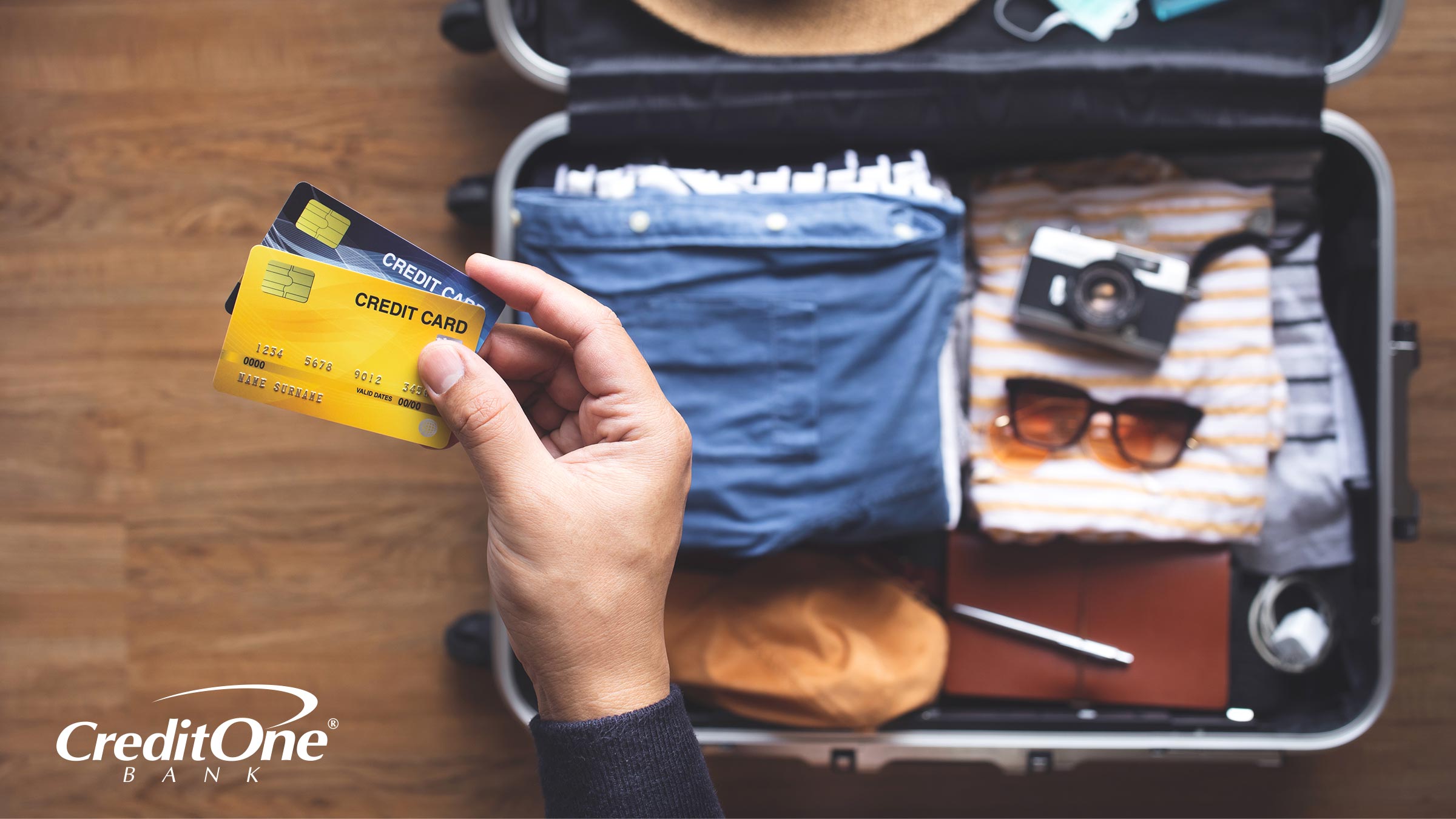 A vacationer holds travel credit cards over his packed suitcase, ready to go on a trip
