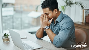 A man is sitting at a laptop, stressed because he doesn’t have credit card payment protection in an emergency.