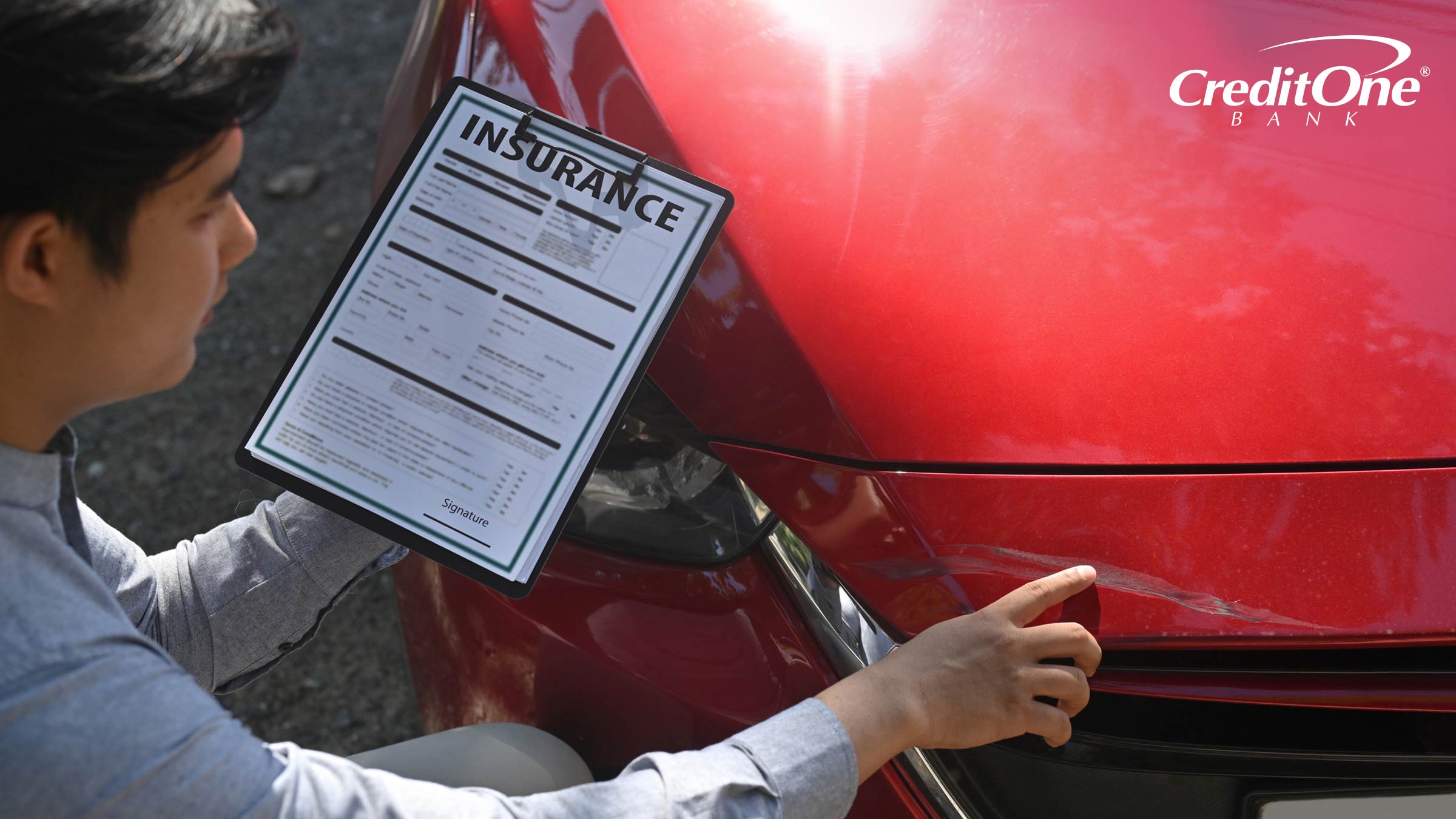 A man holding insurance paperwork assesses a scuff on the front of his red car.