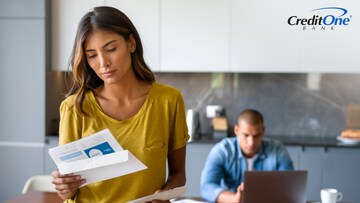 A man works on his laptop as his wife looks at a collections letter, worried about how to remove it from her credit report.