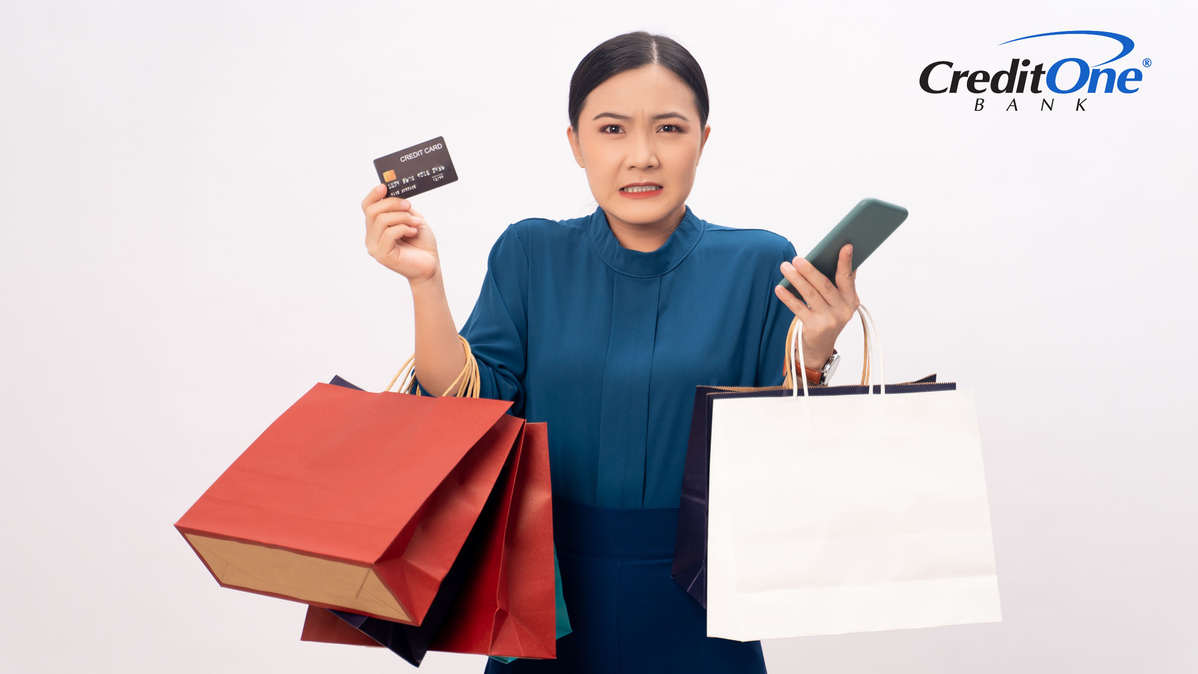 A woman holding shopping bags, a credit card, and a cell phone looks worried about whether she made a good or bad purchase on her card.
