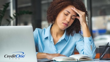 A frustrated businesswoman holds her head in her hand while working, indicating that personal factors have affected her professional life.