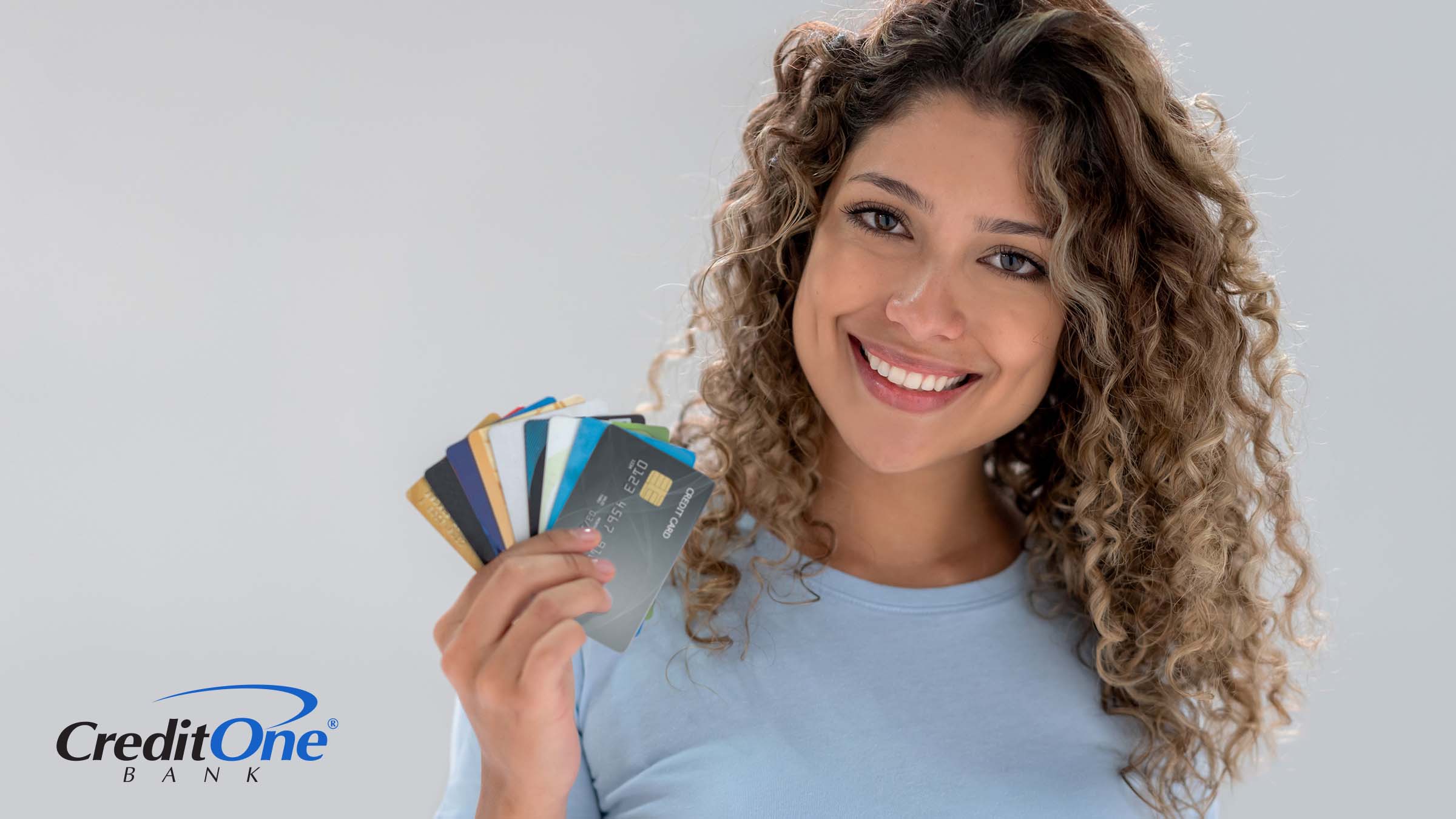 A smiling woman holds a fan of multiple credit cards which she uses for maximum rewards.