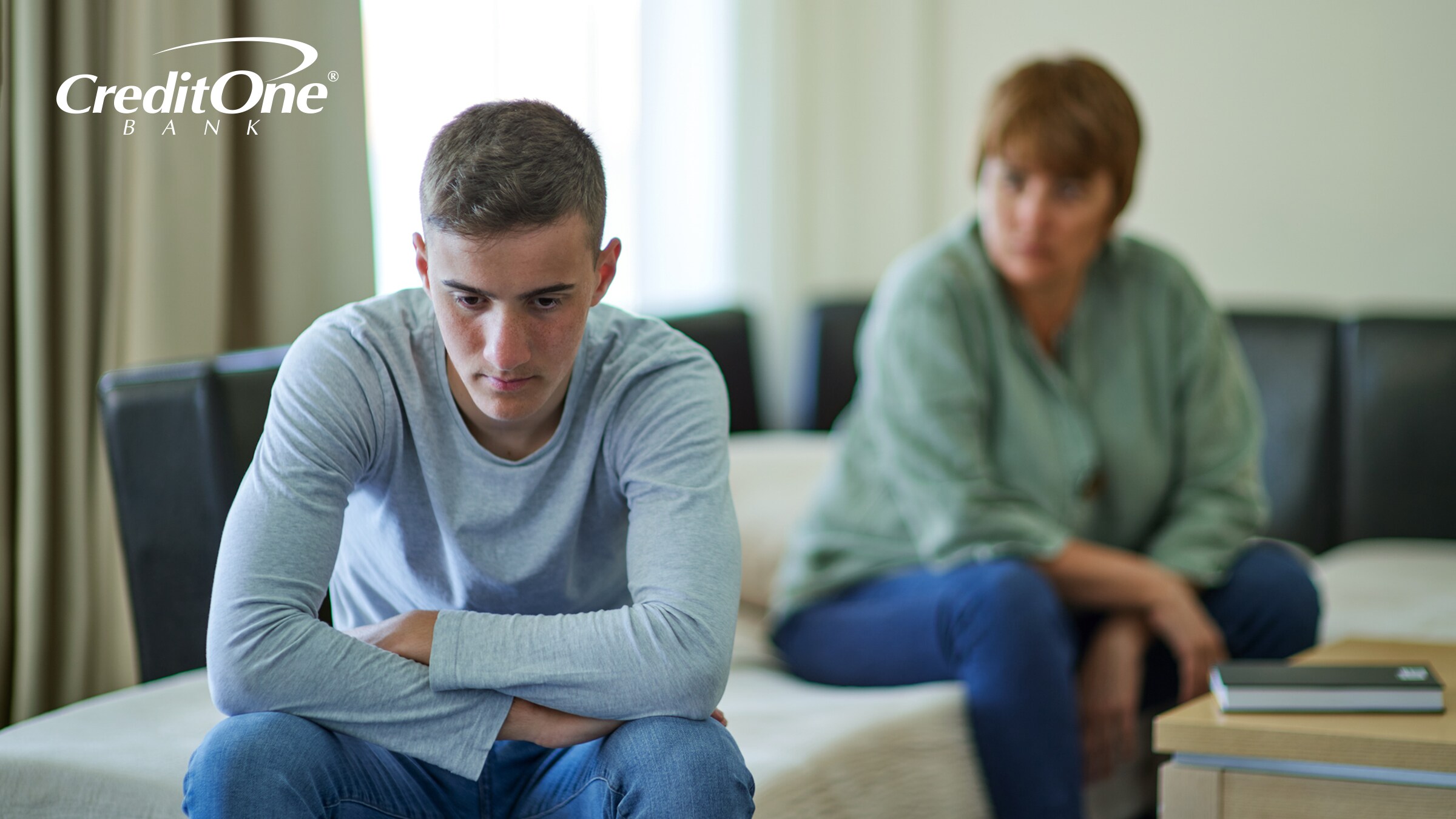 A young man sits with his back turned angrily to his mother, perhaps concerned that she may have harmed his credit.