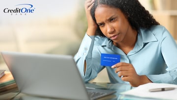 A young woman scowls at her laptop, holding her head in one hand and her credit card in the other, perhaps trying to figure out why her credit score dropped. 