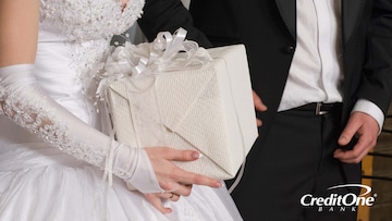 This photo of a bride and groom, shown from the shoulders down, reveals the bride holding a wrapped wedding gift, but we don’t know how much the gift giver spent.