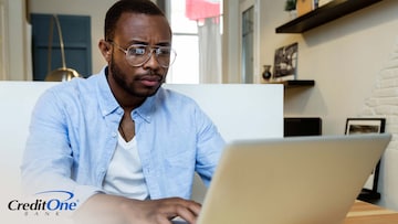A man works on a laptop at his kitchen table, with a determined look on his face as if looking through job postings. If he left his previous job to find new work, this is considered frictional unemployment.