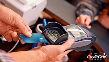 A man’s hands hold a portable credit card reader at a checkout counter while preparing to insert a credit card with an EMV chip.