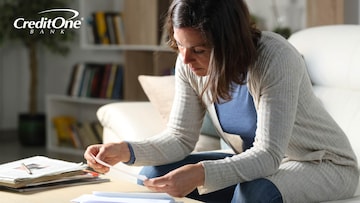 A woman reviews a check while going through her mail, perhaps looking for details like the routing and account numbers.