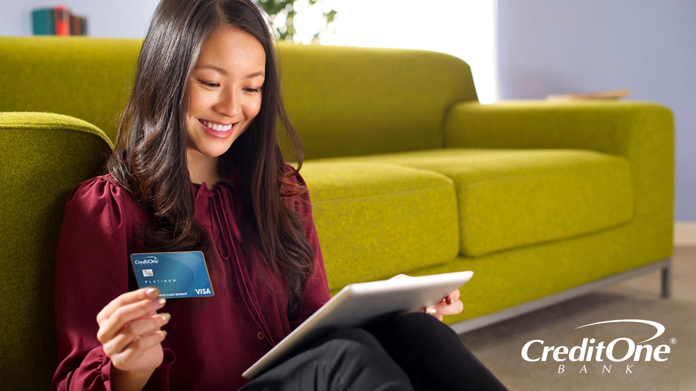 Woman sitting at the base of sofa excited about receiving her first Credit One Visa credit card