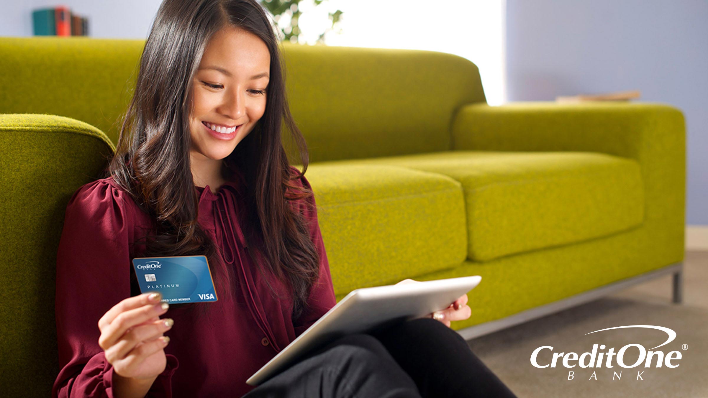 Woman sitting at the base of sofa excited about receiving her first Credit One Visa credit card Woman sitting at the base of sofa excited about receiving her first Credit One Visa credit card