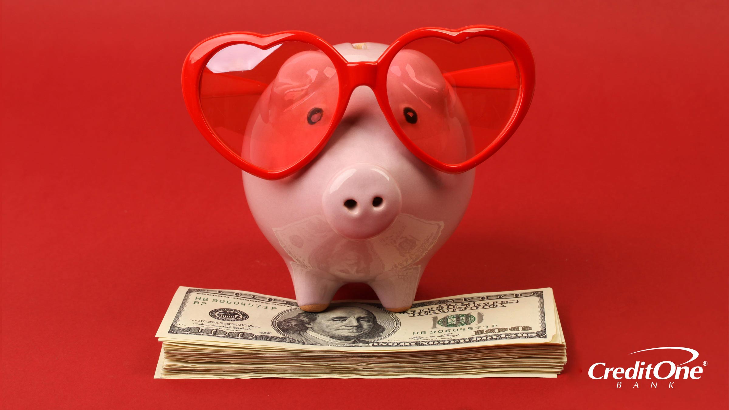 A ceramic piggy bank with heart-shaped glasses sitting on a pile of money