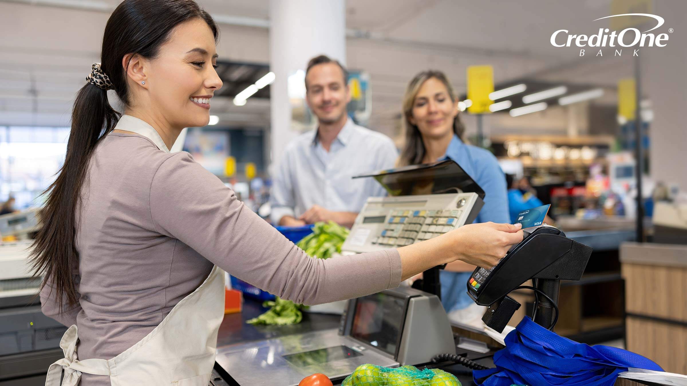 A cashier runs a credit card for a couple buying groceries, triggering a grocery merchant category code A cashier runs a credit card for a couple buying groceries, triggering a grocery merchant category code